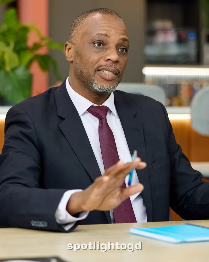 O.G. Dawodu in a dark suit and burgundy tie, speaking in a meeting