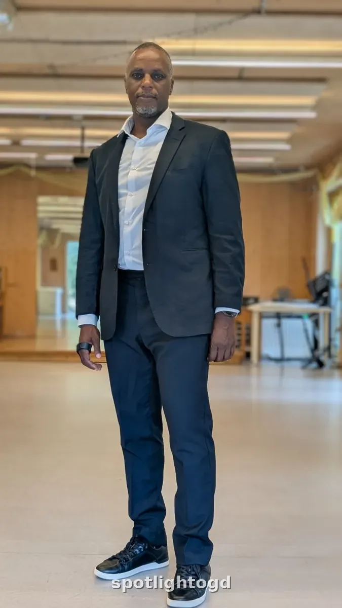 O.G. Dawodu standing full length in a dark blazer, white shirt, dark trousers and black trainers
