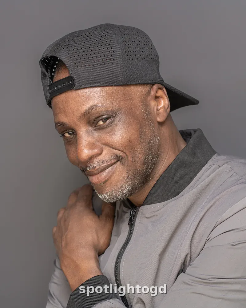 O.G. Dawodu smiling playfully in a backwards cap and grey jacket